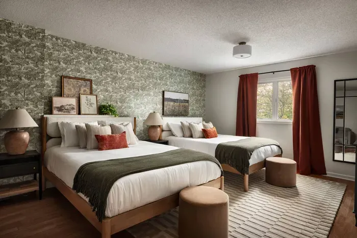 A spacious retreat with two plush queen beds, warm earthy tones, and serene nature-inspired wallpaper—perfect for families or groups.
