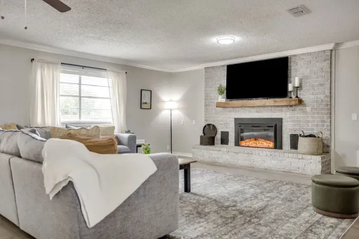 Whitewashed brick fireplace with a wood mantel and a big smart TV above it.