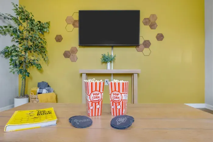 Living room ready for movie night — Smart TV, honeycomb wall décor, yellow accent wall, and popcorn buckets waiting for your crew.
