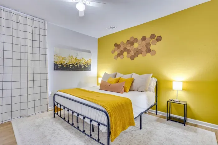 Master bedroom with king bed, bold yellow accent wall, honeycomb wall art, and cozy warm bedding — the heart of The Hive.