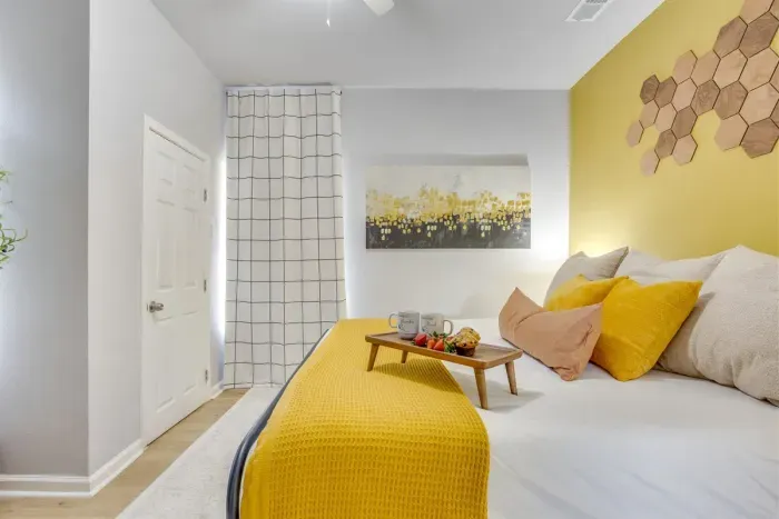 Master bedroom featuring king bed, bold yellow accent wall, grid tile accent wall, and honeycomb décor — thoughtfully designed from floor to ceiling.