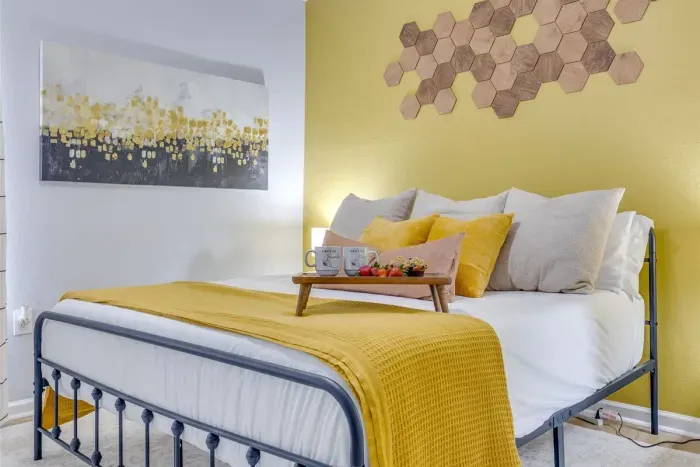 King bed in the master bedroom dressed in yellow and white linens, honeycomb wall décor, and bee-themed accents — cozy, intentional, and one of a kind.