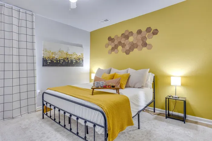Master bedroom with king bed, bold yellow accent wall, honeycomb wall art, grid tile accent wall, and warm yellow bedding — the signature room of The Hive.