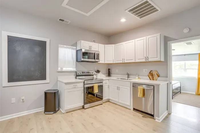 Bright kitchen with stainless appliances, white countertops, and natural light from the back windows — clean, modern, and fully stocked.
