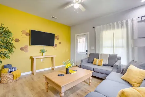 Bright living room with yellow accent walls, Smart TV, sectional sofa with bee-themed décor, and natural light throughout.