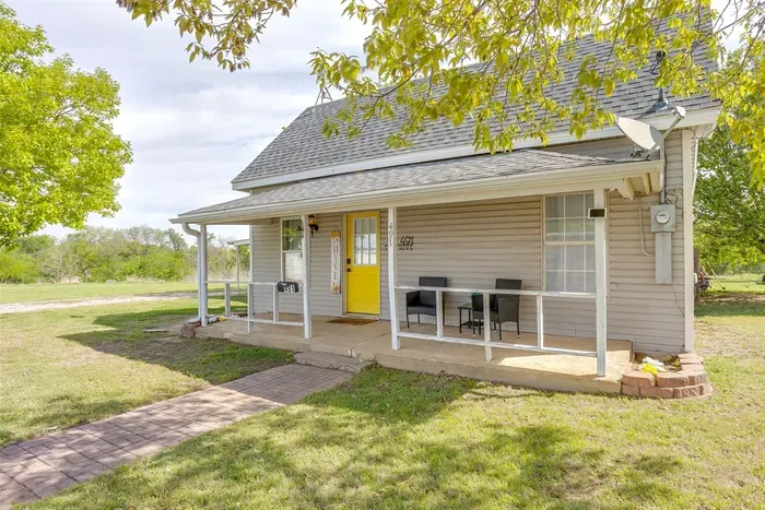 Charming curb appeal with a covered front porch, yellow front door, and mature trees — a welcoming first impression in a quiet Stephenville neighborhood.