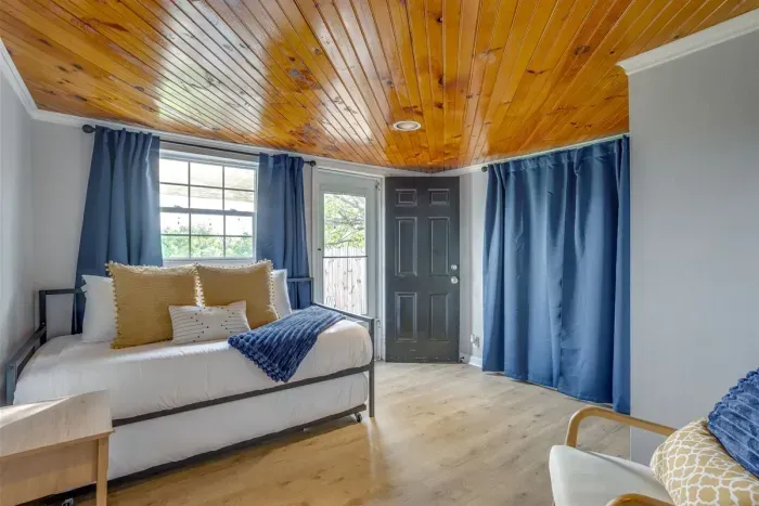 Third bedroom with twin beds, stunning wood plank ceiling, blue curtains, and warm gold accents — a unique and cozy space for kids or extra guests.