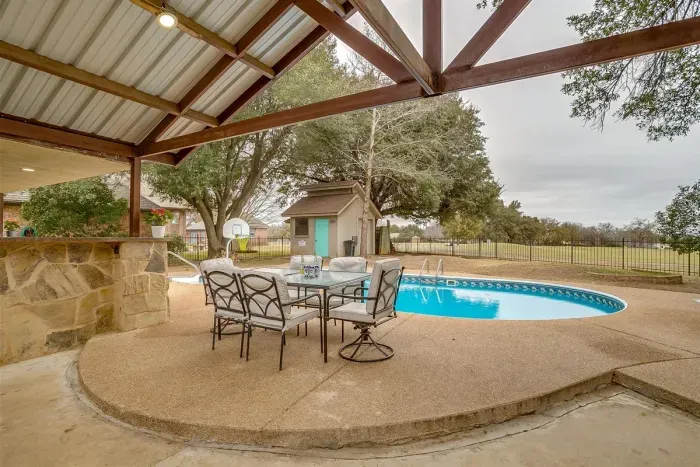 Relax on the covered patio with comfortable seating and a view of the pool, perfect for outdoor dining or starlit evenings