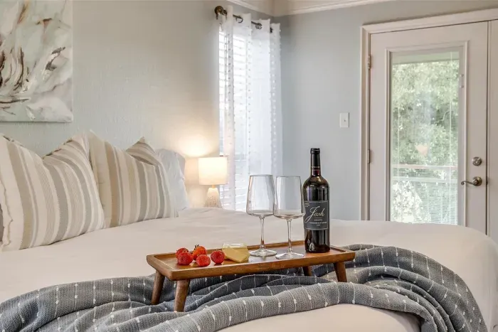 Cozy up in this serene bedroom with plush bedding, elegant decor, and thoughtful touches like a complimentary bottle of wine to welcome you to your stay
