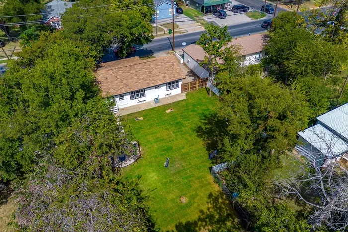 Aerial view of fenced backyard, trees, and play space for kids or pets