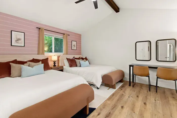 Large primary bedroom with two queen beds, full length mirror, ceiling fan, sliding glass door to backyard, and dedicated work/glam station for two