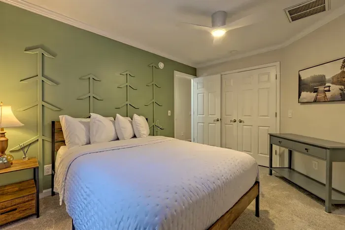 Cozy and charming, this bedroom at Helen Waldhaus features a comfortable queen bed, a serene tree-themed feature wall, a spacious closet, and convenient access to a Jack & Jill bathroom.