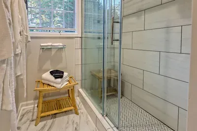 Unwind in this serene bathroom at Helen Waldhaus, featuring a walk-in shower with a spa-like bench, elegant tilework, and plush towels. The large window lets in natural light, creating a relaxing atmosphere for your stay.