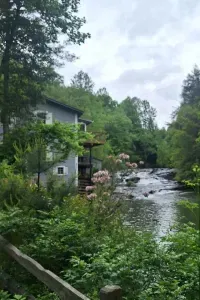 Historic mill beside the cascading Soque River, surrounded by trees and flowering shrubs at Mark of the Potter in Clarkesville