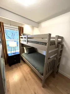 Cozy bunk room with natural light, wood floors, and bedside lamp.