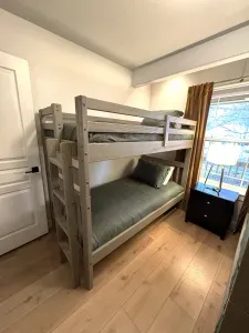 Bright bunk room with twin beds, window light, and bedside lamp