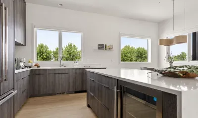 Bright modern kitchen with large island, wine fridge, and sunny tree views