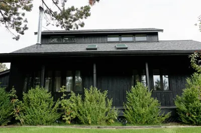 Modern black cabin with covered porch, skylights, and serene wooded setting