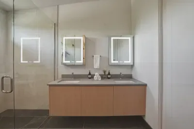 Spa-inspired bathroom with double vanity, lit mirrors, and glass shower
