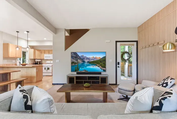 Bright open living room with large TV, cozy seating, and kitchen access