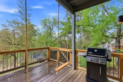 Covered deck with swing and grill in a serene, tree-filled setting