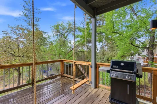 Covered deck with swing and grill in a serene, tree-filled setting