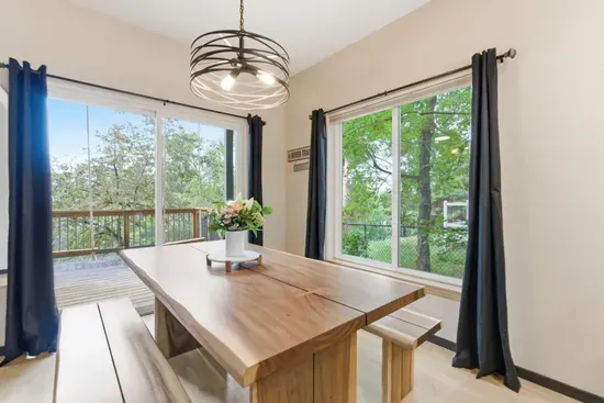 Bright dining space with large windows, deck access, and serene tree views