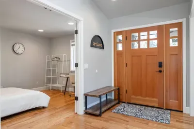 Near the entrance, there is an office/4th bedroom with a desk and chair overlooking the front yard, a queen bed, and standing clothing rack and luggage stand for that 7th or 8th guest.