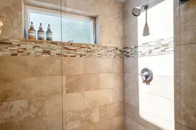 Primary walk in shower is large and luxurious. Outfitted with two shower heads and light pouring in from the skylight above.