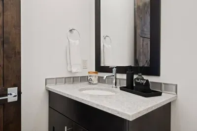 Bathroom 4: Half bathroom (powder room) located downstairs off the main foyer. Includes single vanity sink and toilet. Bathrooms come with towels, hand soap, and jar of hair ties and cotton balls.