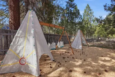 Fenced forest play zone with swings and teepee forts for kids