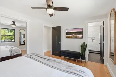 Sunny modern bedroom with ensuite bath, TV, arched mirror and closet.