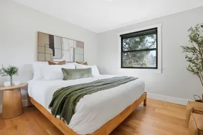 Serene, light-filled bedroom with king bed, hardwood floors, and view.