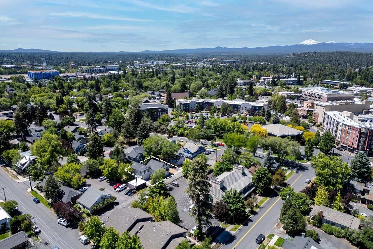 Aerial drone view of Greeley Cottage in a Bend, OR neighborhood with mature trees and snow-capped mountains, Mountain Haus