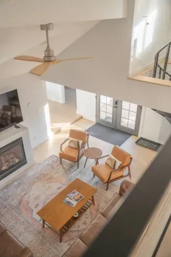 Bright vaulted living room with fireplace, leather seating, and airy loft view