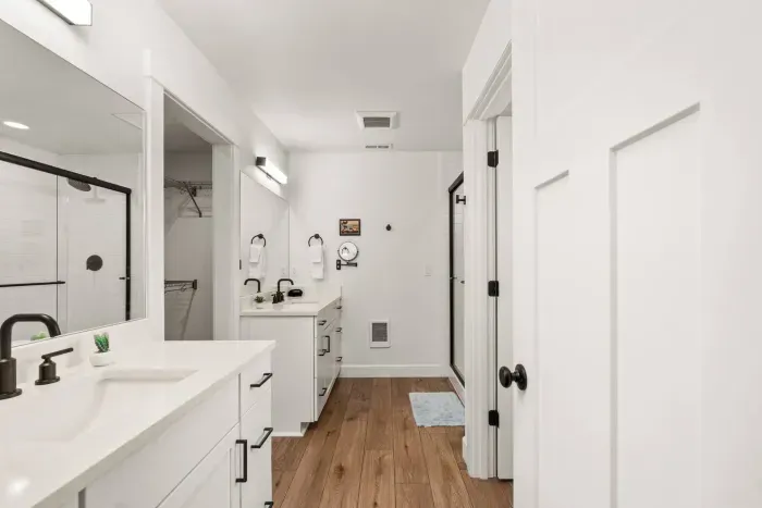 Bright modern bath with dual vanity, glass shower, and warm wood floors