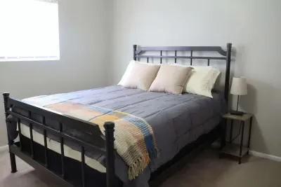 Queen bed with metal frame, nightstand, and natural light from window.
