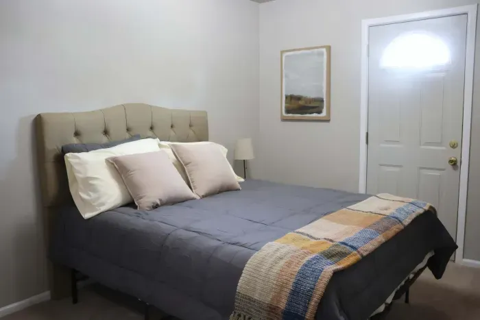 Queen bed with tufted headboard and bedside lamp.