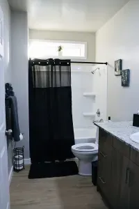 Full bathroom with tub-shower combo, storage shelves, and natural light from window.