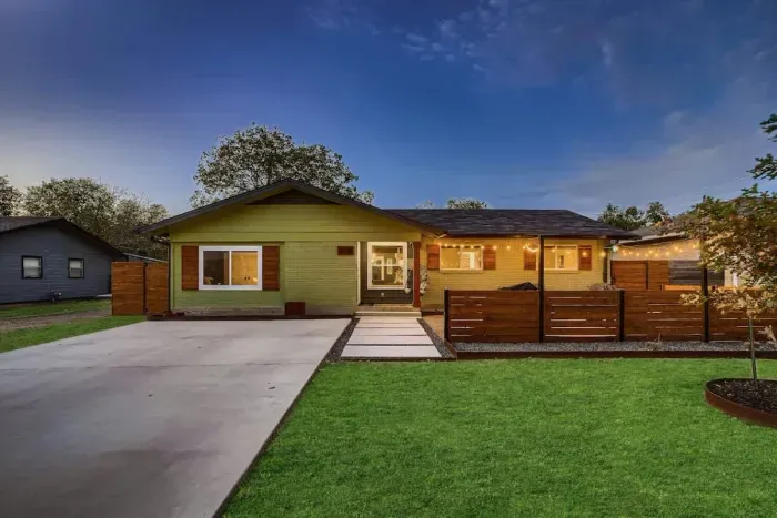 Admire the front exterior in the evening, where warm lights highlight the vibrant apple green color of the house. The well-manicured lawn complements the scene, with a touch of blue sky adding to the serene ambiance.