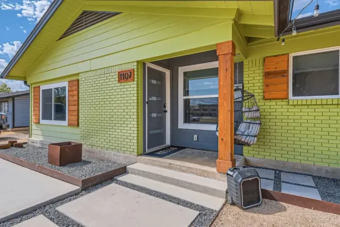 The front exterior of the house, bathed in daylight, showcases its vibrant green color, standing out with a bold, fresh appeal. The bright hue is complemented by well-maintained landscaping, creating a welcoming and energetic atmosphere.