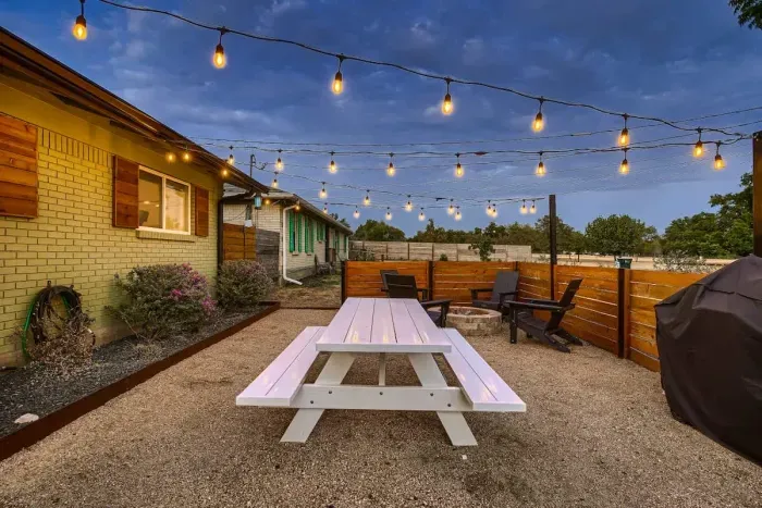 Experience the amazing outdoor space in the front, beautifully lit for a cozy ambiance. The fenced area features a rustic wooden table, perfect for dining or relaxing while enjoying the serene surroundings.