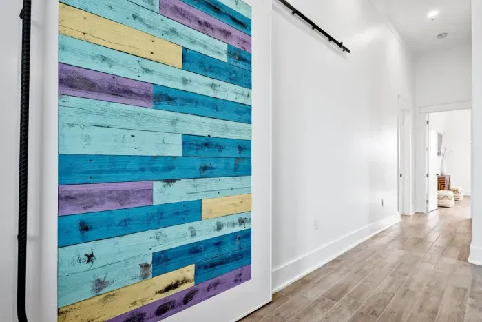 A vibrant sliding barn door with distressed wood planks in bold blues, purples, and yellows adds a striking contrast to the sleek, modern hallway.