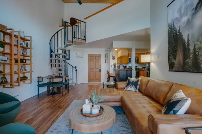 A gorgeous living room accented by a rustic spiral staircase, high ceilings, and designer mountain-home styling.