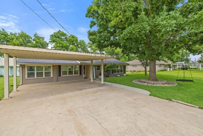 Front exterior with a neat driveway and shaded trees.