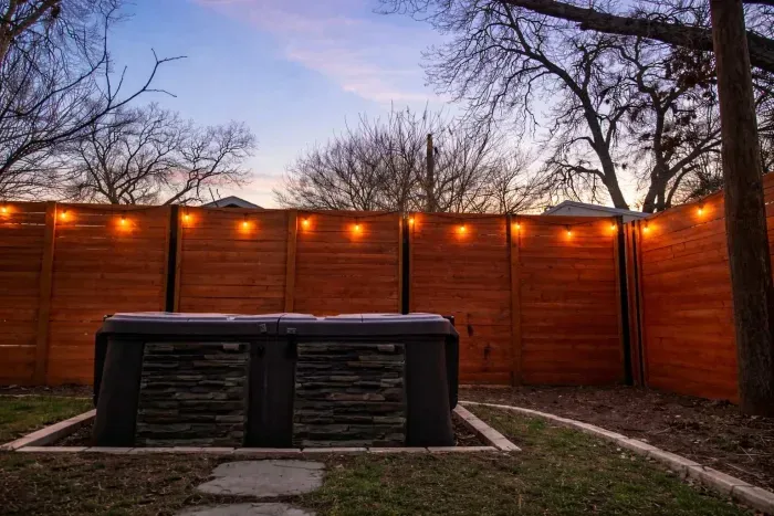 Private spa surrounded by wood fencing and soft evening string lights.