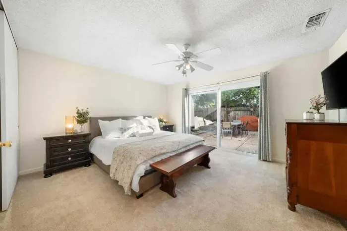 Spacious primary bedroom with plush bedding, ceiling fan, and direct backyard access.