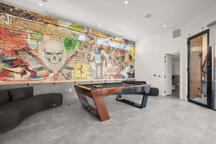Enjoy a one-of-a-kind game room featuring a custom mural, modern pool table, and stylish lounge seating.