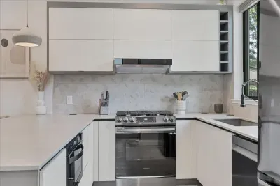 Side view of this modern kitchen with custom handmade pendant lights, gas stove, dishwasher, under counter microwave, refrigerator, and large single basin sink. Flat front modern  European cabinets.