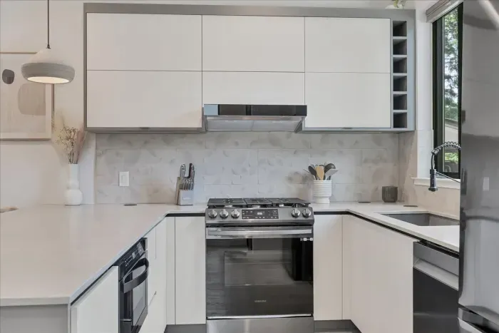 Side view of this modern kitchen with custom handmade pendant lights, gas stove, dishwasher, under counter microwave, refrigerator, and large single basin sink. Flat front modern  European cabinets.